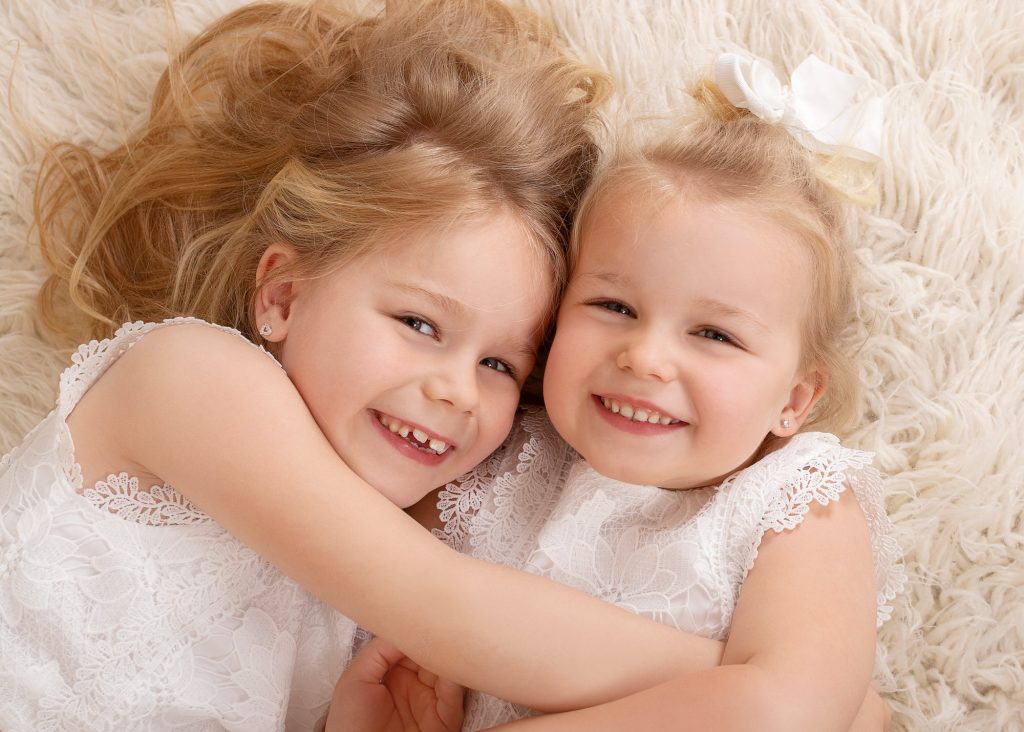 sisters laying on a fluffy run laughing taken by Kent newborn photographer