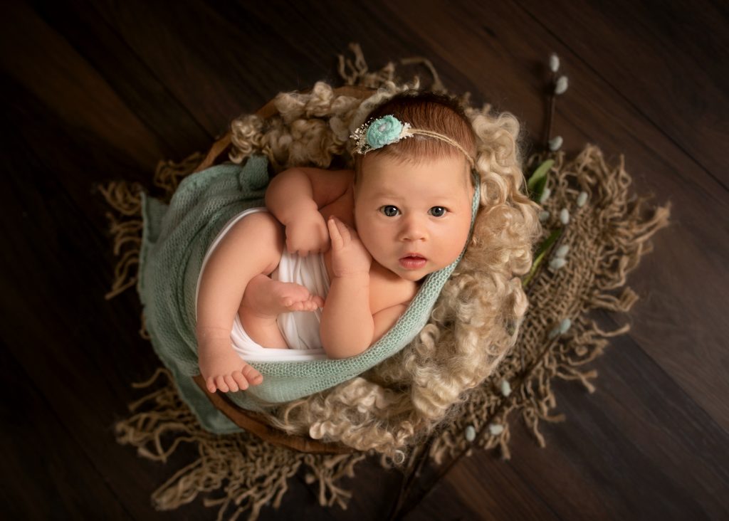 newborn baby girl wide eyed in bowl with green wrap photographed in Kent