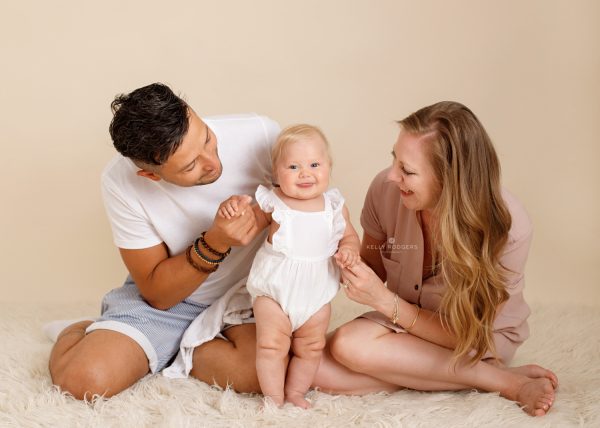 baby dressed in white romper suit holding mum and dads hand photographed in Kent