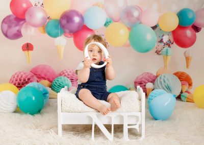 boys first birthday holding a wooden letter, sat on a wooden bed with balloons
