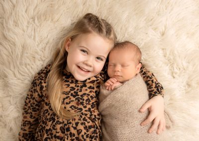 sister and newborn baby brother laying on a cream rug during newborn photoshoot in Kent