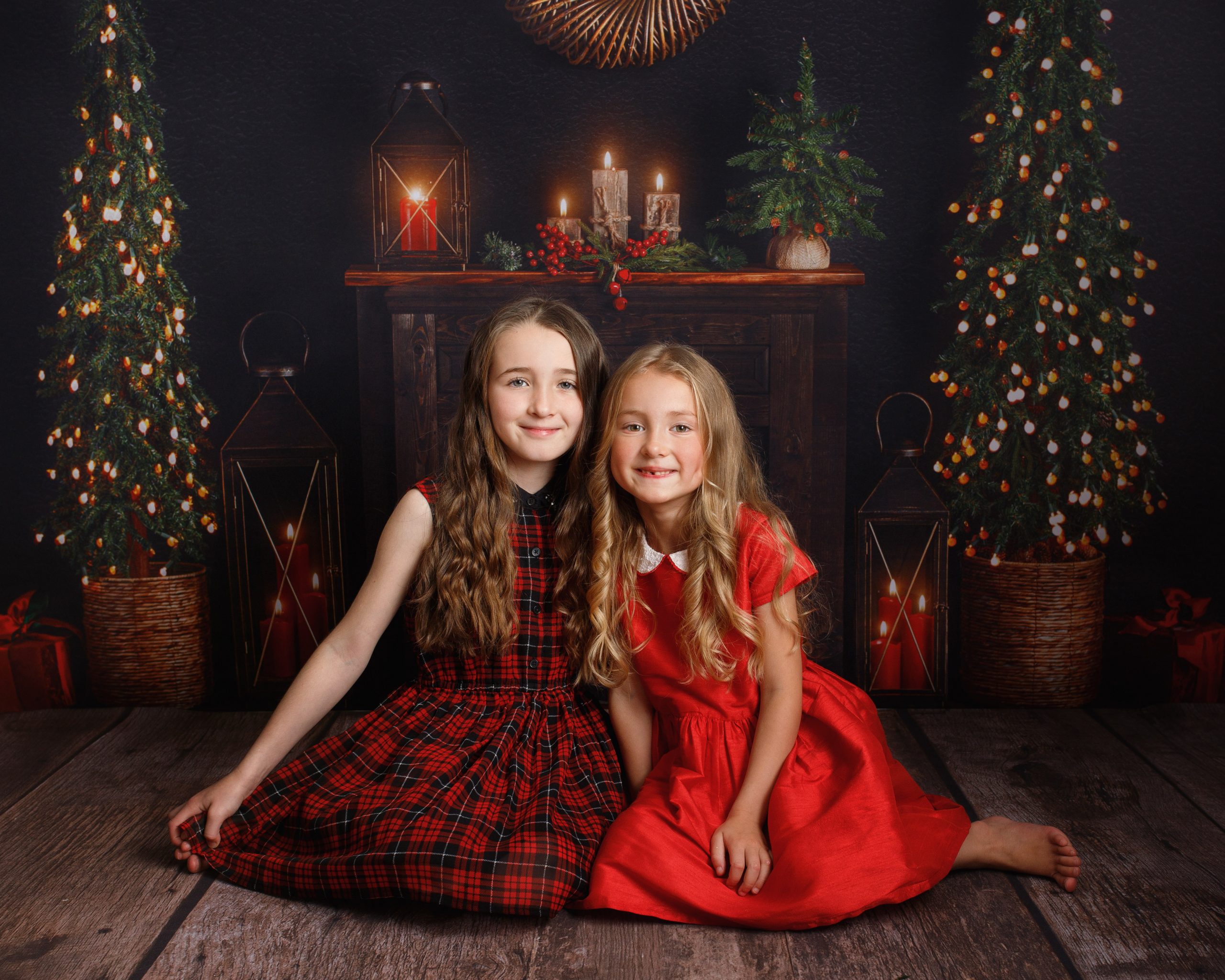two girls, one in tartan dress, one in red dress sitting for a Christmas photoshoot in Kent