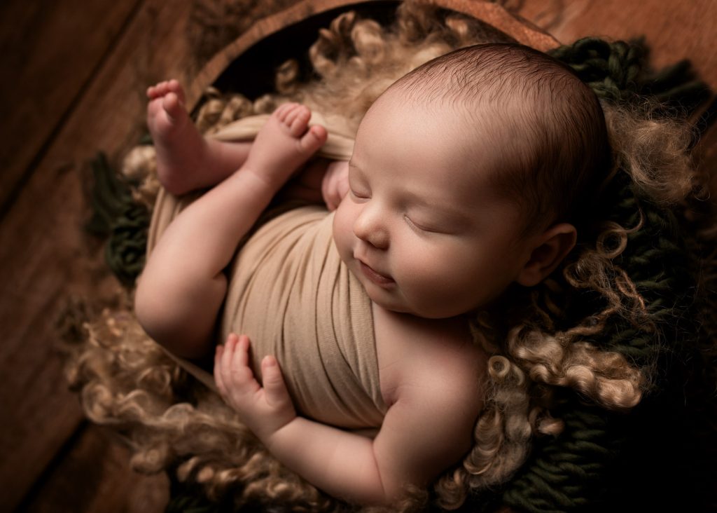 baby boy curled up in wooden bowl during a photography session in Kent