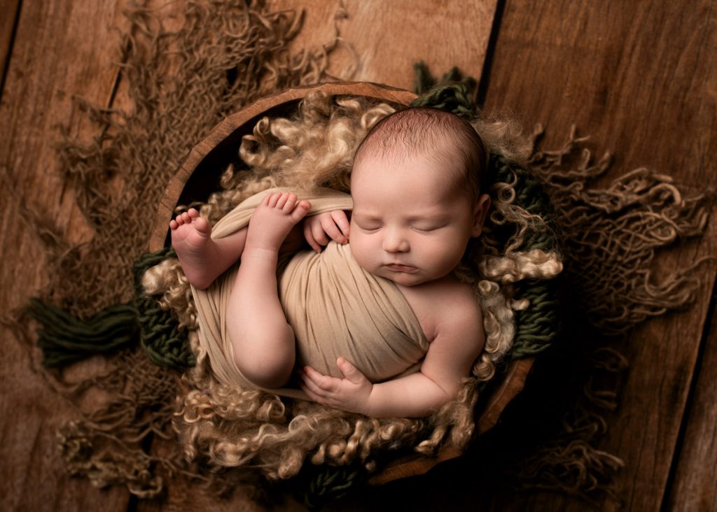 baby boy curled up in wooden bowl during a photography session in Chatham