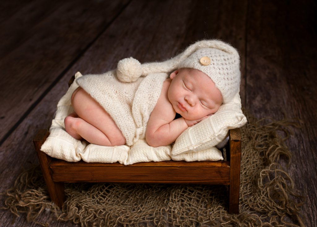 baby curled up asleep on wooden bed during a newborn photography session in Kent