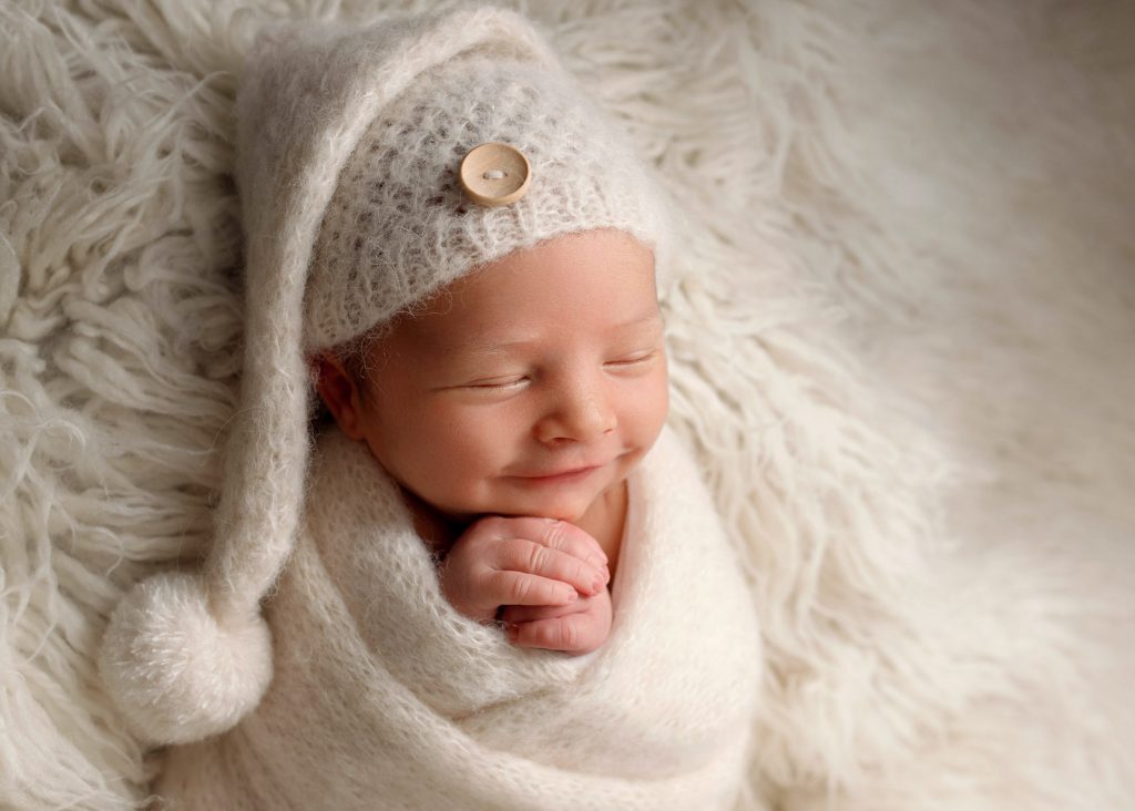 baby with a knitted bobble hat smiling during a photoshoot in Chatham