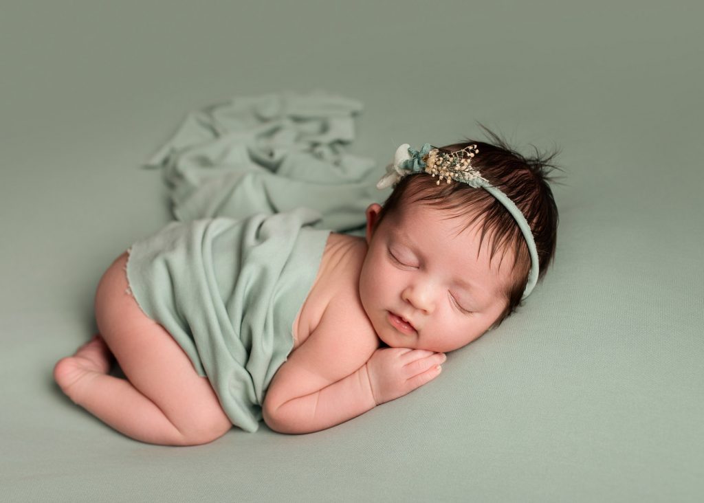 newborn baby girl laying on a green blanket during photoshoot in kent