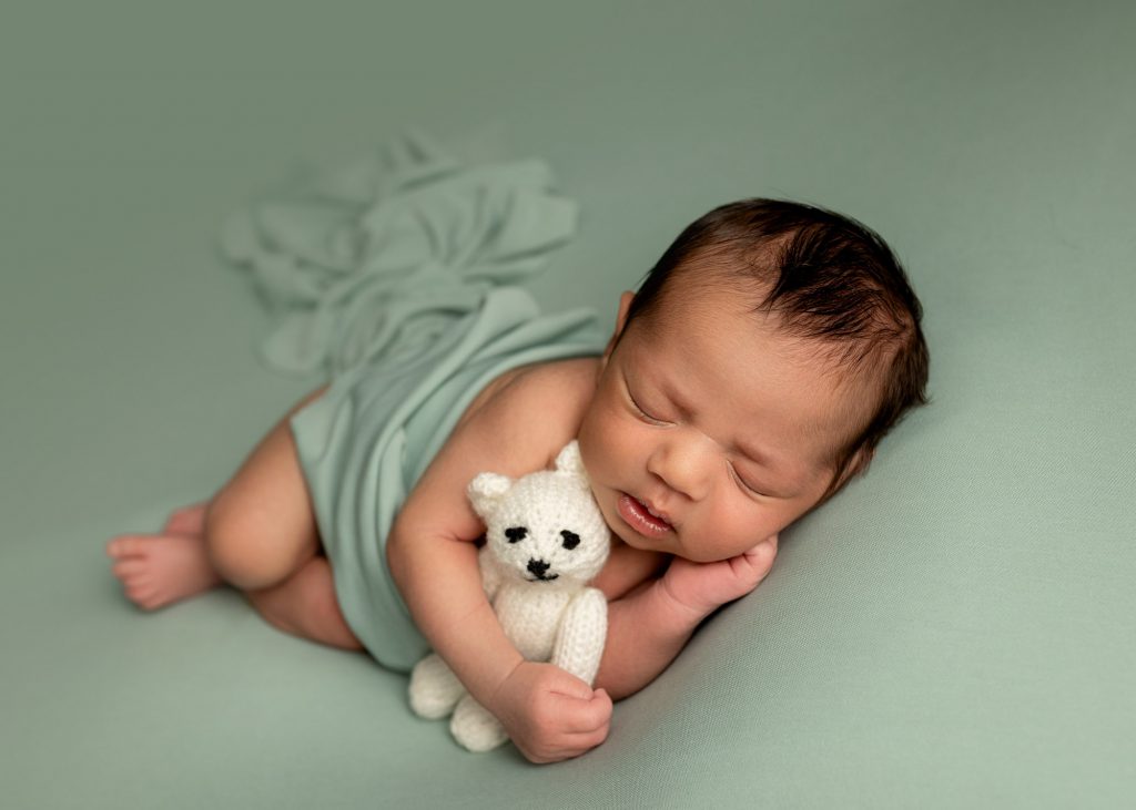 baby boy cuddling a teddy photographed on a green blanket during a photoshoot in Kent