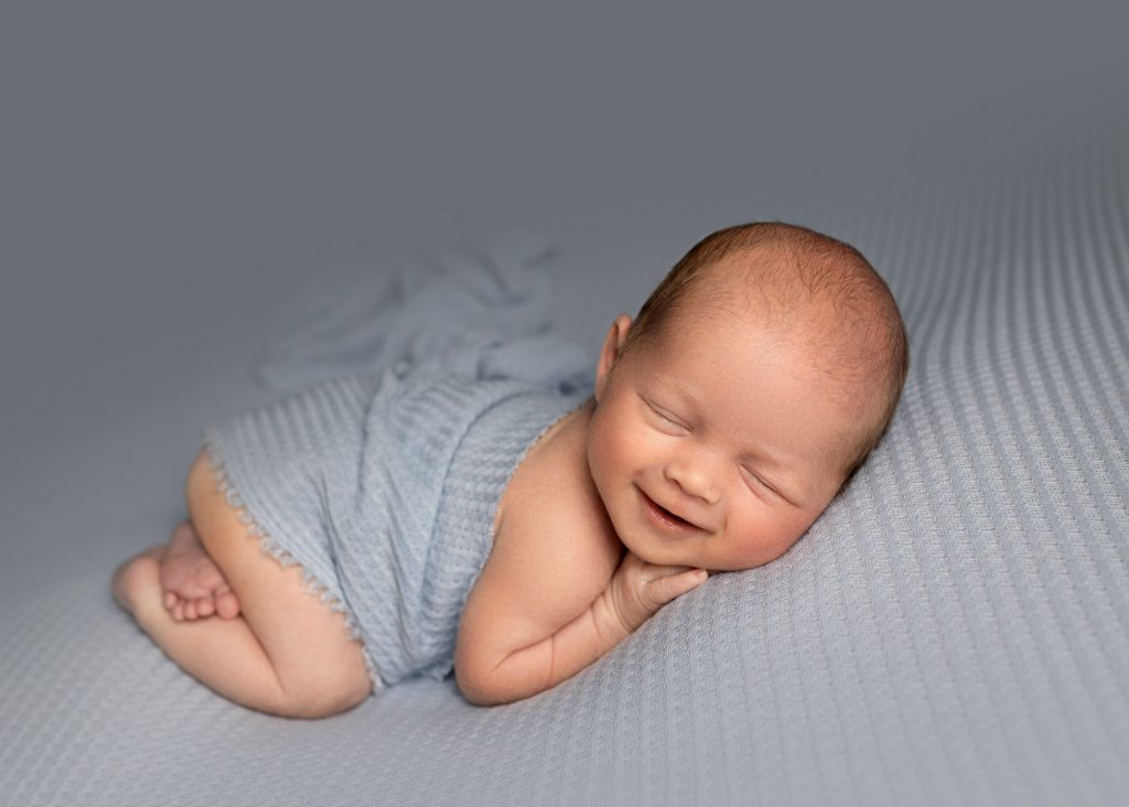 newborn baby boy laying on a blue blanket smiling during a photoshoot in kent