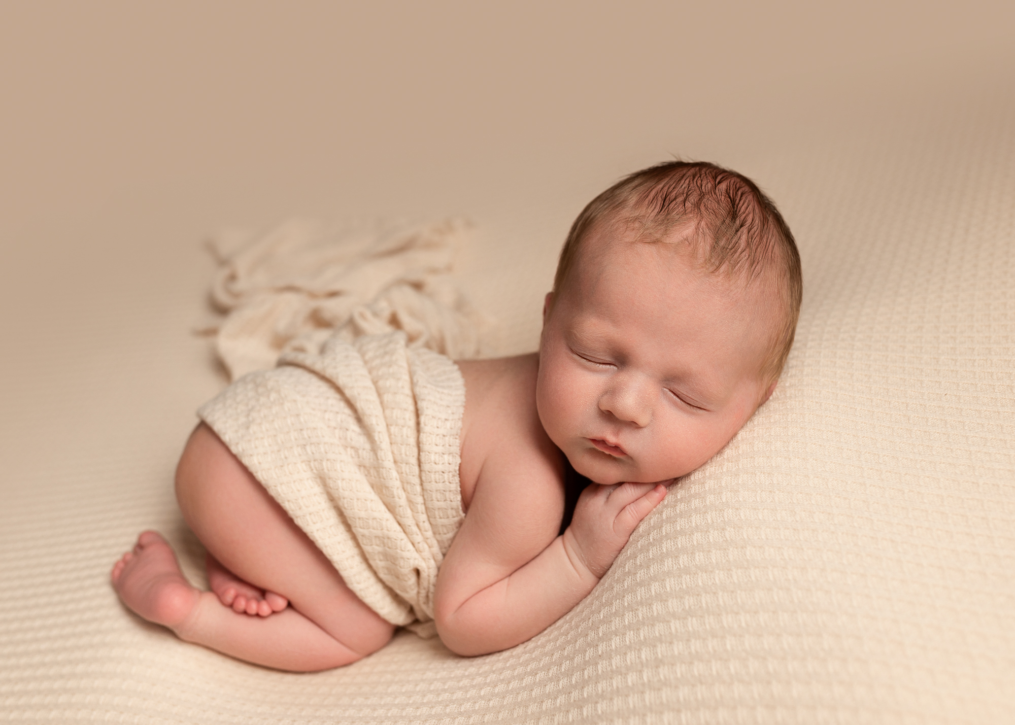 newborn baby curled up asleep on cream blanket during a newborn photoshoot in Kent