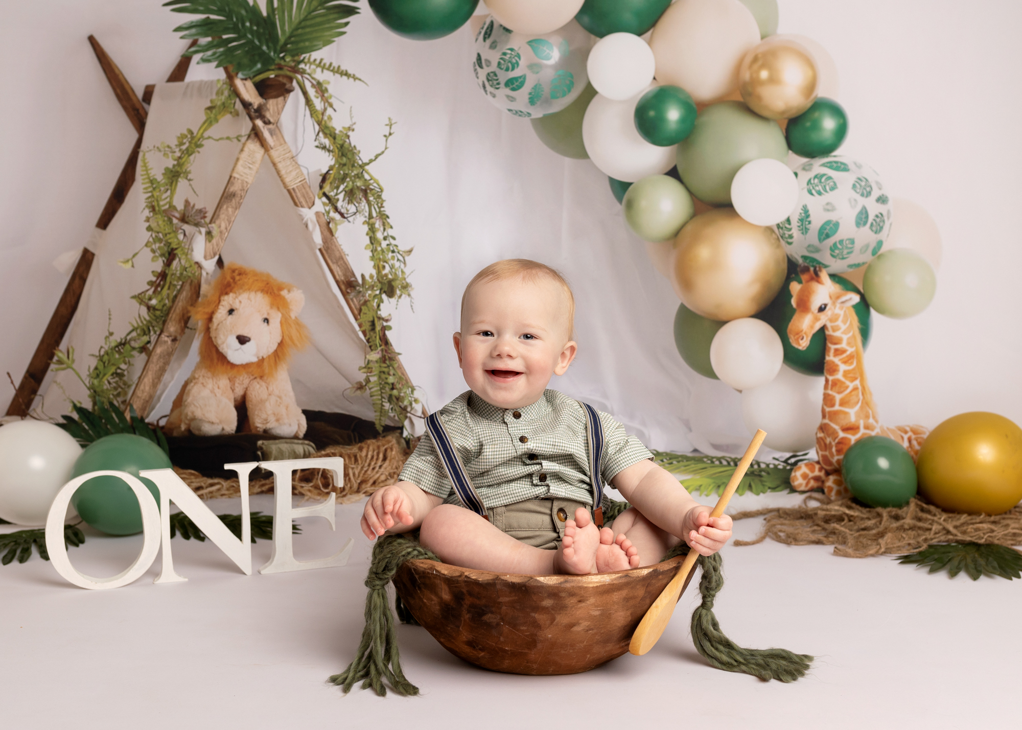 Baby boy sat in a bowl with a jungle theme backdrop during a cake smash photoshoot