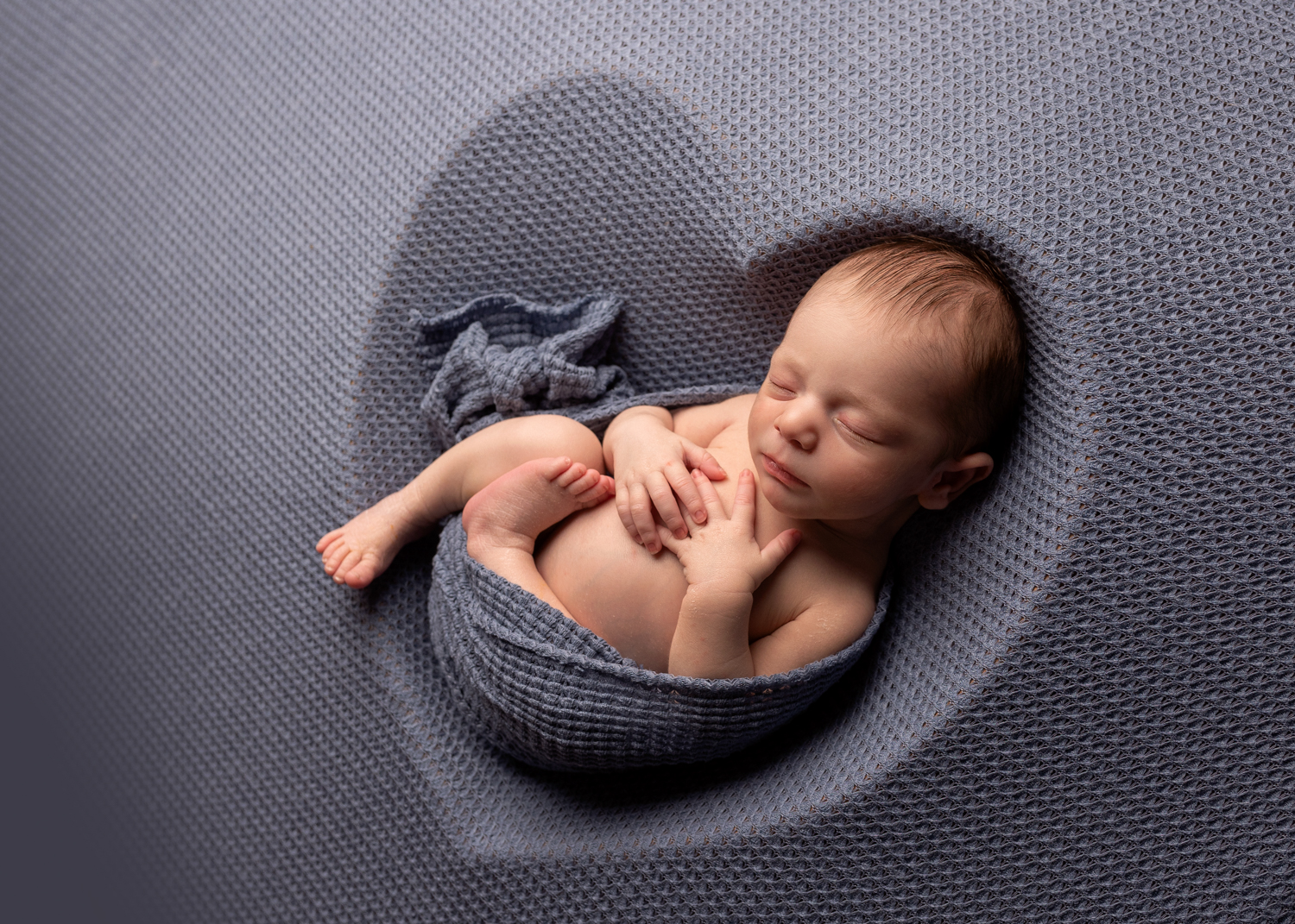 newborn baby boy laying in a heart shaped blue blanket during a newborn photoshoot in Kent