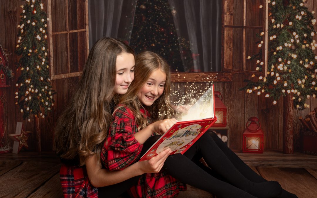 sisters looking at a Christmas book with magic sparkle flying out during a photoshoot in Kent